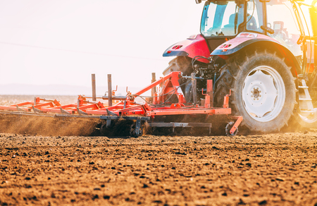 Farmer in tractor preparing land with seedbed cultivator as part of pre seeding activities in early spring season of agricultural works at farmlands.の写真素材