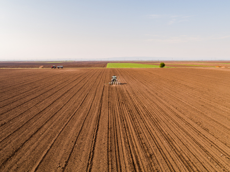 Aerial shot of a farmer seeding, sowing crops at field. Sowing is the process of planting seeds in the ground as part of the early spring time agricultural activities.の写真素材
