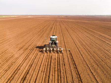 Aerial shot of a farmer seeding, sowing crops at field. Sowing is the process of planting seeds in the ground as part of the early spring time agricultural activities.の写真素材