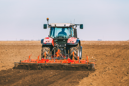 Farmer in tractor preparing land with seedbed cultivator as part of pre seeding activities in early spring season of agricultural works at farmlands.の写真素材