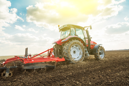 Farmer in tractor preparing land with seedbed cultivator as part of pre seeding activities in early spring season of agricultural works at farmlands.の写真素材