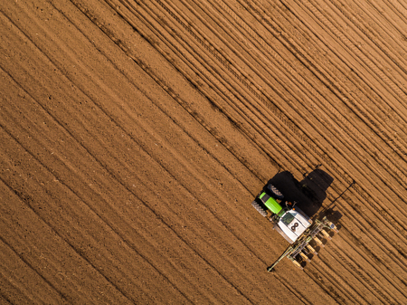 Aerial shot of a farmer seeding, sowing crops at field. Sowing is the process of planting seeds in the ground as part of the early spring time agricultural activities.の写真素材