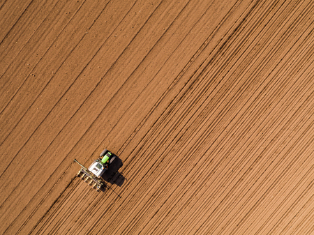 Aerial shot of a farmer seeding, sowing crops at field. Sowing is the process of planting seeds in the ground as part of the early spring time agricultural activities.の写真素材
