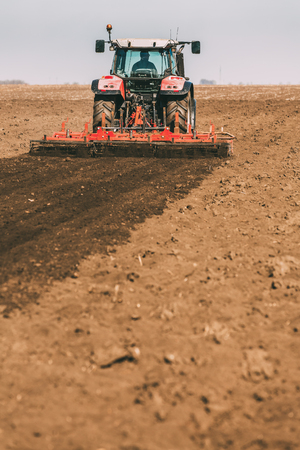 Farmer in tractor preparing land with seedbed cultivator as part of pre seeding activities in early spring season of agricultural works at farmlands.の写真素材