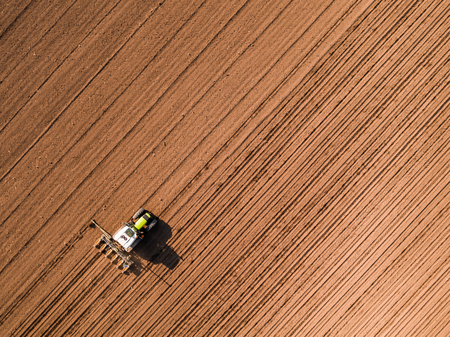Aerial shot of a farmer seeding, sowing crops at field. Sowing is the process of planting seeds in the ground as part of the early spring time agricultural activities.の写真素材