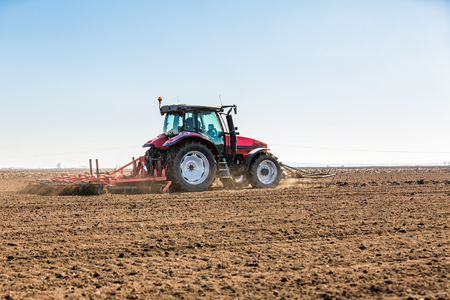 Farmer in tractor preparing land with seedbed cultivator as part of pre seeding activities in early spring season of agricultural works at farmlands.の写真素材
