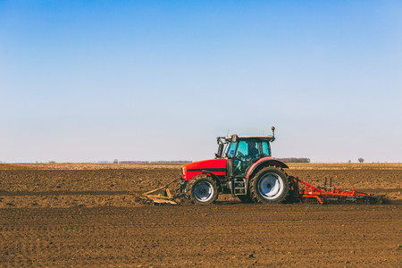 Farmer in tractor preparing land with seedbed cultivator as part of pre seeding activities in early spring season of agricultural works at farmlands.の写真素材