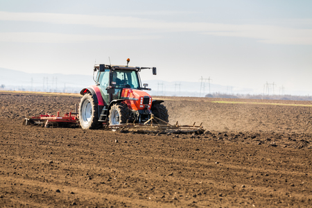 Farmer in tractor preparing land with seedbed cultivator as part of pre seeding activities in early spring season of agricultural works at farmlands.の写真素材