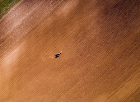 Aerial shot of a farmer seeding, sowing crops at field. Sowing is the process of planting seeds in the ground as part of the early spring time agricultural activities.の写真素材