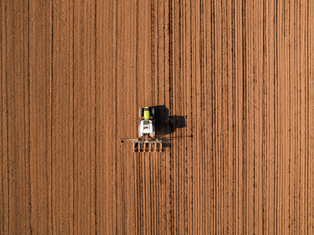 Aerial shot of a farmer seeding, sowing crops at field. Sowing is the process of planting seeds in the ground as part of the early spring time agricultural activities.の写真素材