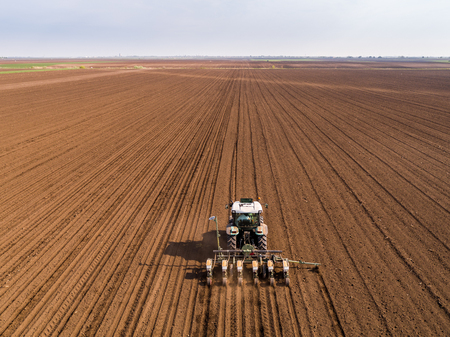 Aerial shot of a farmer seeding, sowing crops at field. Sowing is the process of planting seeds in the ground as part of the early spring time agricultural activities.の写真素材