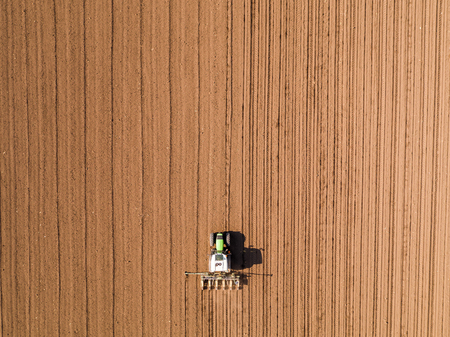 Aerial shot of a farmer seeding, sowing crops at field. Sowing is the process of planting seeds in the ground as part of the early spring time agricultural activities.の写真素材