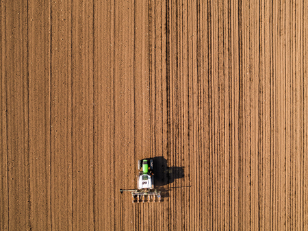 Aerial shot of a farmer seeding, sowing crops at field. Sowing is the process of planting seeds in the ground as part of the early spring time agricultural activities.の写真素材