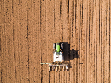 Aerial shot of a farmer seeding, sowing crops at field. Sowing is the process of planting seeds in the ground as part of the early spring time agricultural activities.の写真素材