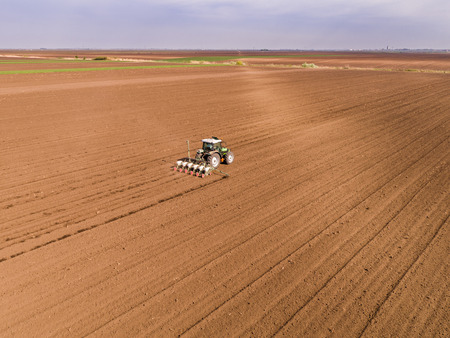 Aerial shot of a farmer seeding, sowing crops at field. Sowing is the process of planting seeds in the ground as part of the early spring time agricultural activities.の写真素材