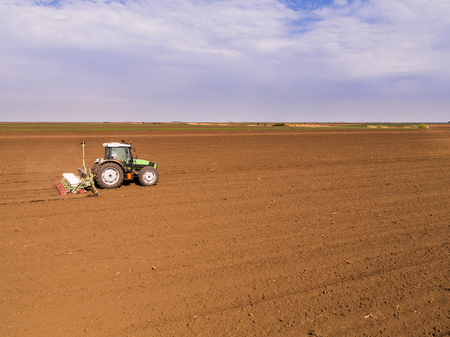 Aerial shot of a farmer seeding, sowing crops at field. Sowing is the process of planting seeds in the ground as part of the early spring time agricultural activities.の写真素材
