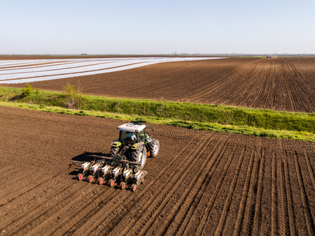 Aerial shot of a farmer seeding, sowing crops at field. Sowing is the process of planting seeds in the ground as part of the early spring time agricultural activities.の写真素材