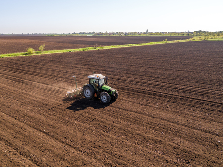 Aerial shot of a farmer seeding, sowing crops at field. Sowing is the process of planting seeds in the ground as part of the early spring time agricultural activities.の写真素材