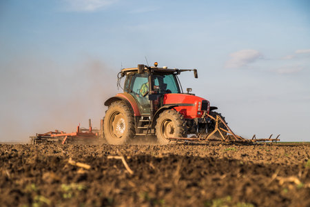 Farmer in tractor preparing land with seedbed cultivator as part of pre seeding activities in early...