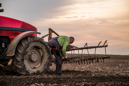 Farmer in tractor preparing land with seedbed cultivator as part of pre seeding activities in early spring season of agricultural works at farmlands.の写真素材