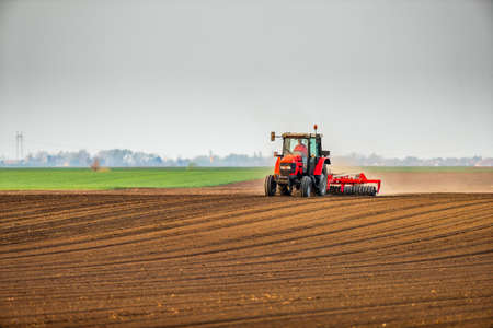 Farmer in tractor preparing land with seedbed cultivator as part of pre seeding activities in early spring season of agricultural works at farmlands.の写真素材