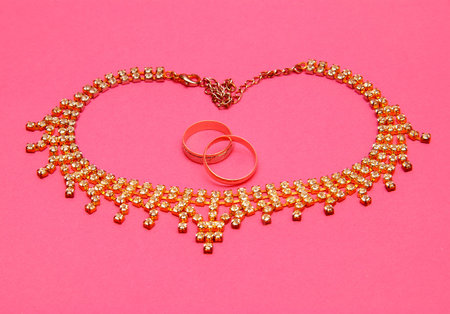 Two wedding rings and heart from the chain on a pink backgroundの写真素材