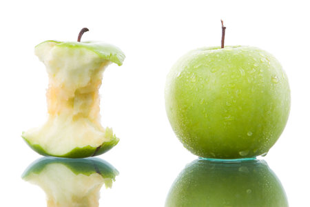 Fresh and bitten green apple side by side on glass table.の写真素材