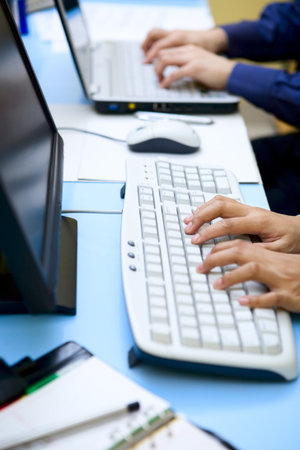 Showing only hand is typing in front of the computer and laptop.