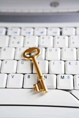 A golden key placed on the keyboard of a laptop. Very shallow depth of field, focus mainly on the tip of the key.の写真素材