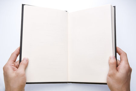 Hand holding opened book at blank page. There is soft vignette on the corner and the light is set at...