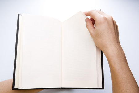 A hand is flipping the page of a book. Clean and empty page to put any words there. There is soft vignette on the corners and set the light in the middle to enhance the effect.の写真素材