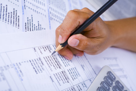 From side high angle view of a hand holding a pencil checking financial report.
