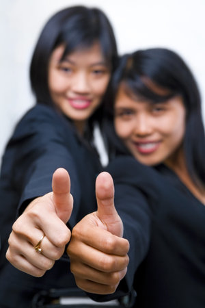 Both young businesswoman showing thumb up, focus mainly on the fingers.の写真素材