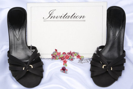 Card with 'invitation' word printed on it and placed between high heels and necklace placed in front...
