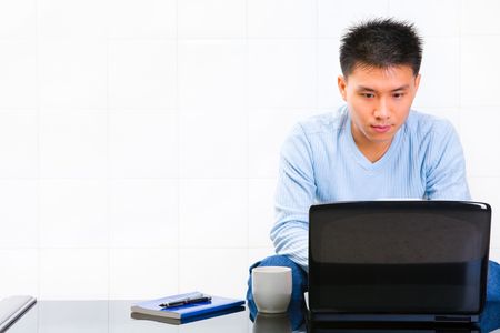 A young man using his laptop with lot of copy space on his right.の写真素材