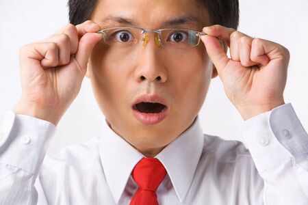 A young Asian businessman gazing at camera while holding glasses to camera with surprised expressionの写真素材