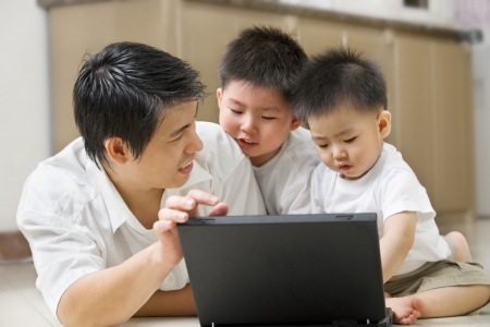 Father introduce technology to his sons using laptop in homeの写真素材