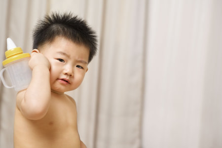 Asian toddler and nipple bottle with such expression in bed room, enough copy spaceの写真素材