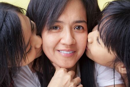 both girls kissing their mother from left and right sideの写真素材