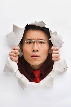 Man gazing seriously from hole in wallの写真素材