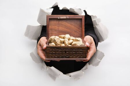 Hand breakthrough wall holding golden nuggets in treasure chest means breakthrough in finance or similar things - one of the breakthrough seriesの写真素材