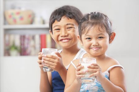 Two little boy and girl each holding a glass of milk and looking at cameraの写真素材