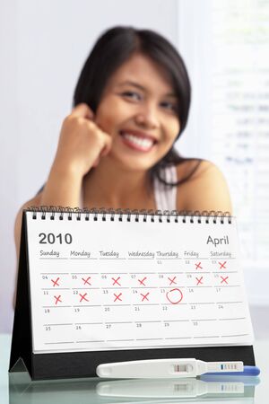 Happy woman with positive pregnancy test and calendar. A concept being sucess to get pregnantの写真素材