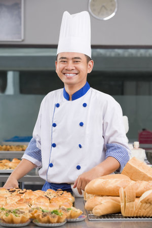 Asian chef or baker posing in front of the pastries in the commercial kitchen