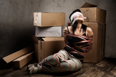 A young woman tied-up, blind folded and muted in old room. Low key settingの写真素材