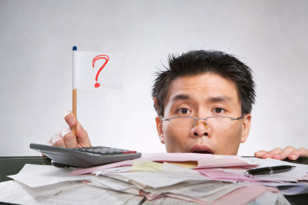 Man holding question mark flag made of paper and pencil with lots of bills in front of him