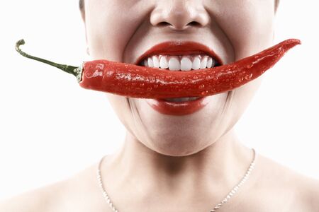Woman holding big red chili in her mouth mouthの写真素材