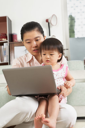 Mother and daughter playing with laptop together at homeの写真素材