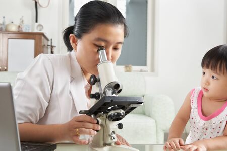 Little Chinese girl trying to distract her mom concentration from working on microscopeの写真素材