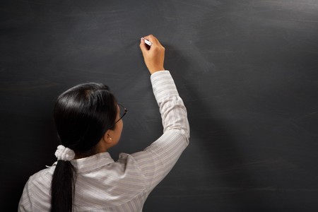 Female teacher holding chalk on blank blackboardの写真素材